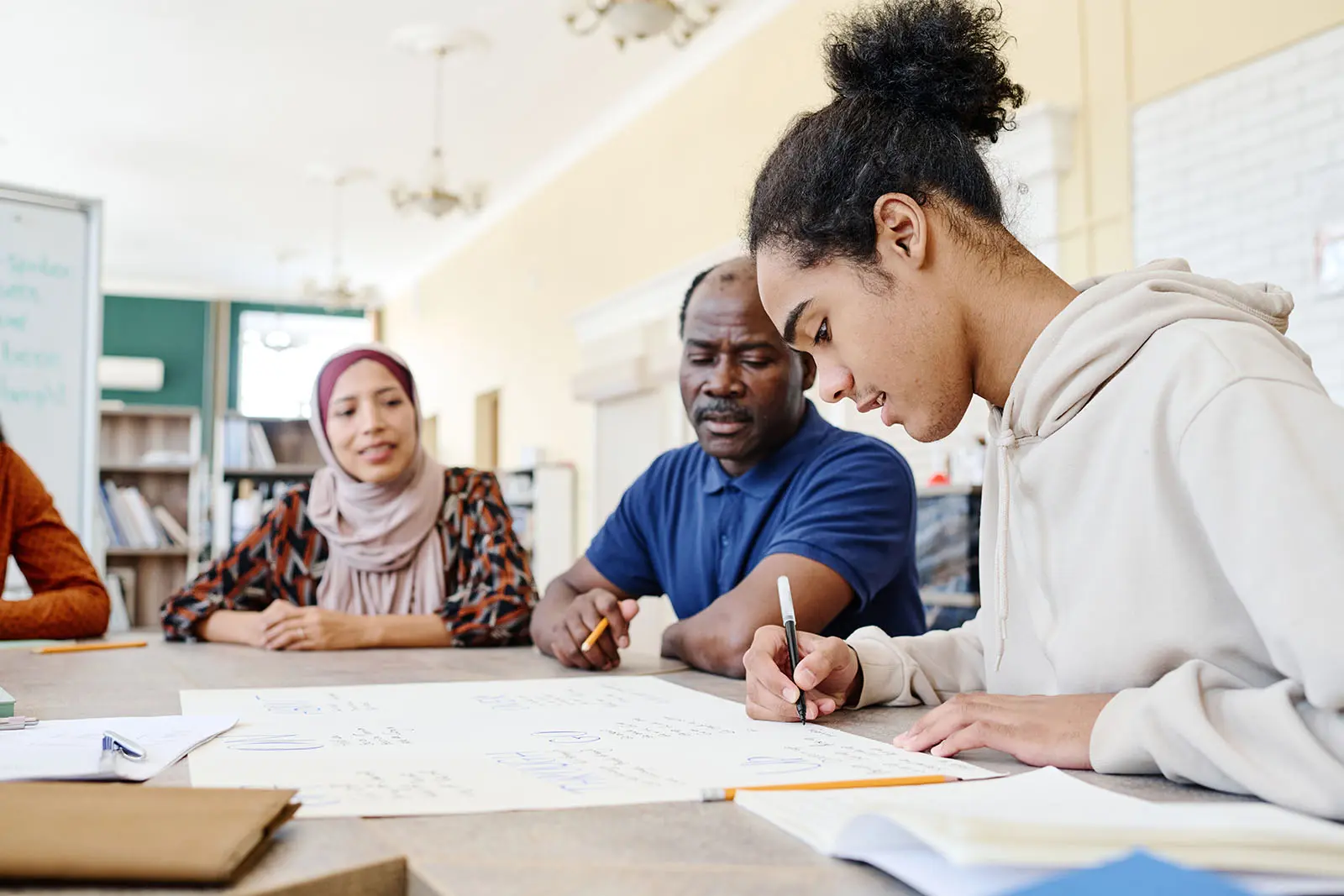 A diverse group of people are seated at a table in what appears to be an educational setting.